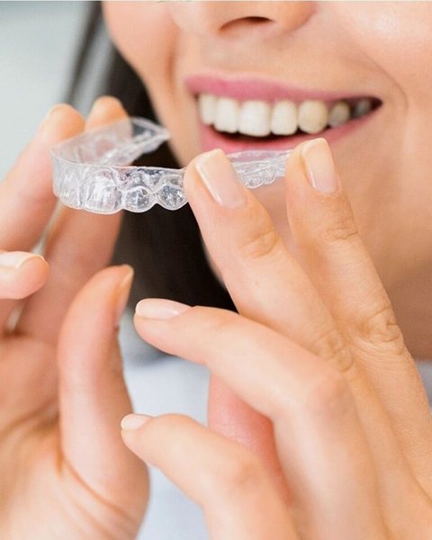Mulher sorrindo, tranquila, com o alinhador transparente na mão